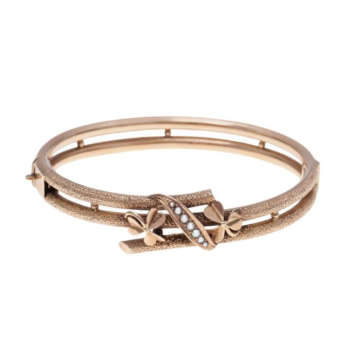 Antiker Armreif in 585er Rotgold wohl um 1900 mit schauseitig 2 Kleeblättern geschmückt sowie ein geschwungenes Band mit 7 kleinen Saatperlen. Der Armreif besteht aus 2 Bögen, die auf der oberen Seite zu 3 Bögen geteilt werden. 