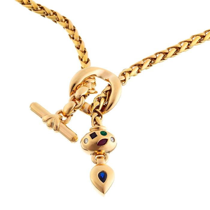 Collier aus 14-karätigem Gelbgold. Zwei Elemente sind mit Edelsteinen bestückt. Das ovale trägt 2 Brillanten, einen Smaragd, einen Rubin und einen Saphir. Das andere Element trägt einen Saphir. 