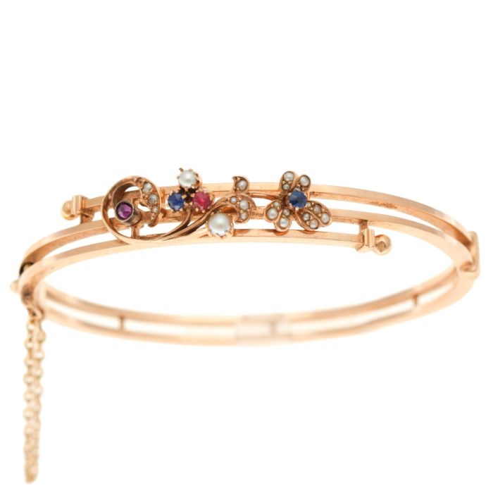 Roséfarbener Jugendstil-Armreif in 585er Gelbgold in gedrehter Form. Schauseitig hat er einen filigran gearbeiteten Aufbau mit einem floralen Design, das mit Saatperlen und natürlichen Rubinen und Saphiren bestückt ist. 
