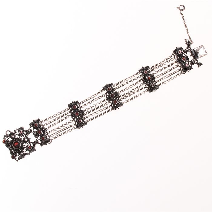 Trachtenschmuck. Der Steckverschluss ist gleichzeitig die Schauseite des Armbandes. 
Typische Trachtenmuster mit Granaten zieren das Schmuckstück. Zwischen den einzelnen Gliedern sind jeweils 6 Kettchen in Erbsgliederform mit Ösen befestigt.