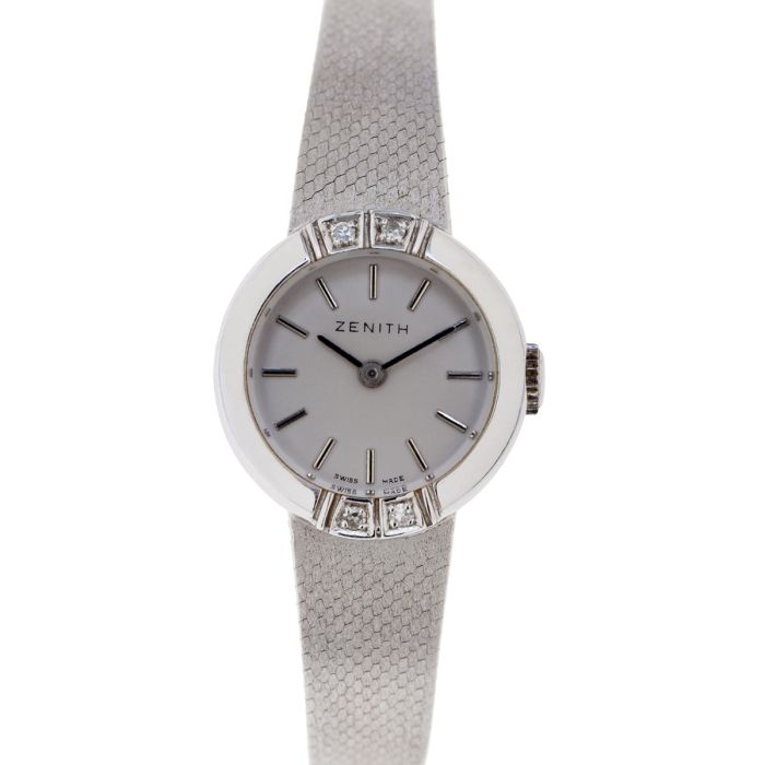 Damen-Armbanduhr von Zenith um 1960/65, poliertes schwach bombiertes Gehäuse auf der Lünette oben und unten besetzt mit je zwei Diamanten im Achtkantschliff zus. ca. 0,05 ct. (Weiß), Zifferblatt mit Strichen als Indizes. Massives Schmuckband im Verlauf sc